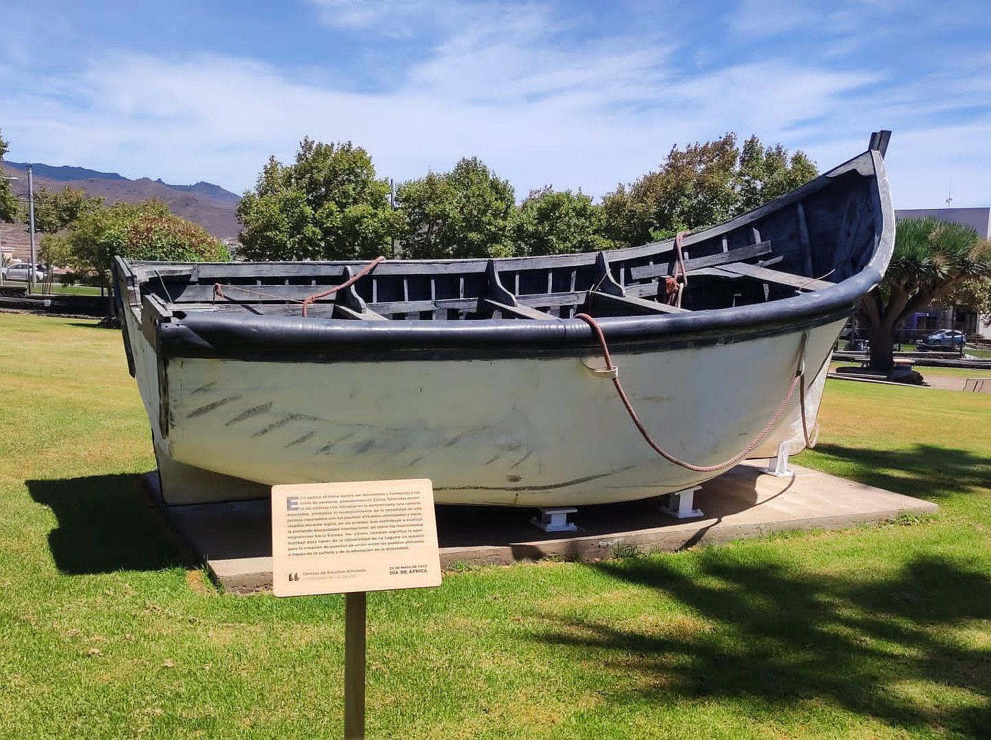 An installation of a boat on a lawn, with a sign in front of it, to commemorate the migrants that died at sea. ©Private Image by Mirco Buoso.