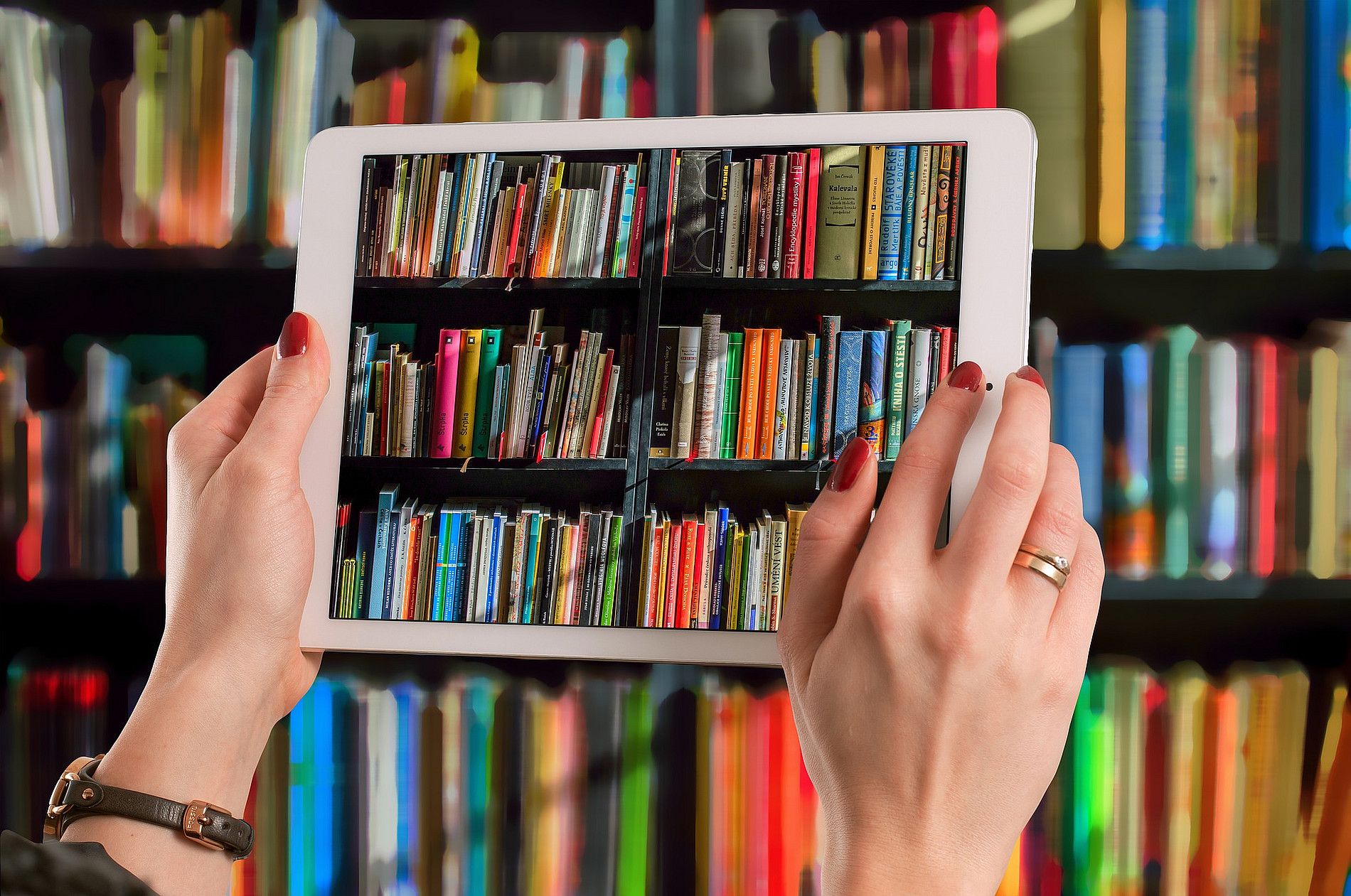 A bookshelf in the background, a person holds a tablet in front of the bookshelf and shows the same books on the screen, symbolizing scripts and publications. ©Pixabay Lizenz/Gerd Altmann 