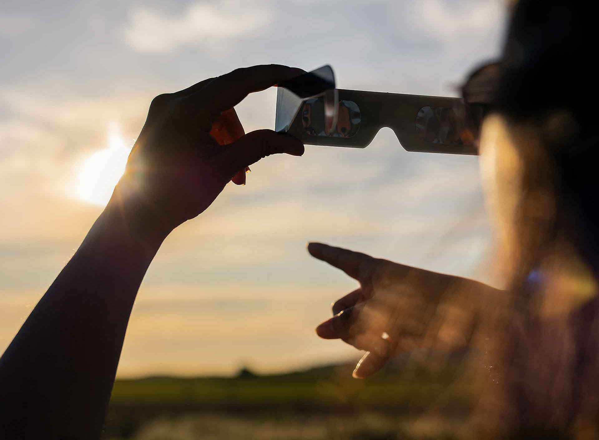Eine Person hält eine Brille in der Hand und hält sie gegen die Sonne 