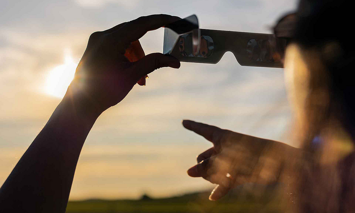 Eine Person hält eine Brille in der Hand und hält sie gegen die Sonne