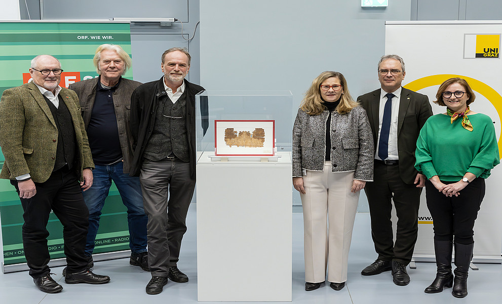 Ein Gruppenfoto an der Universität Graz, sechs Personen stehen nebeneinander, in der vorderen Mitte befindet sich ein altes Papyrusobjekt im Glas