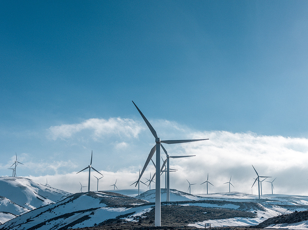 Windkraftanlagen auf verschneiten Bergen unter strahlend blauem Himmel während des Tages ©by Jason Blackeye on unsplash