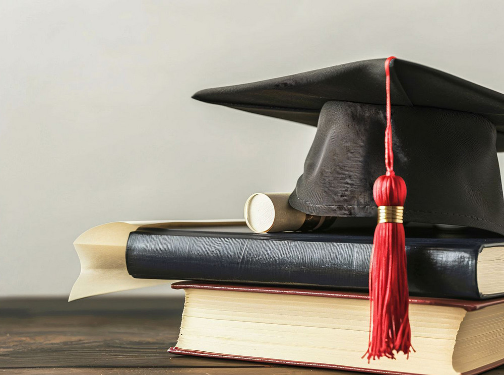 Abschlusshut mit Diplom und Büchern auf dunklem Tisch ©Anas - stock.adobe.com