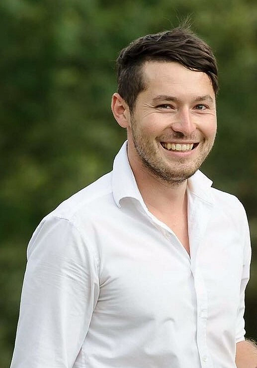 Fotografie von Paul Krenn, USW Geo-Absolvent, lachend in weißem Hemd.