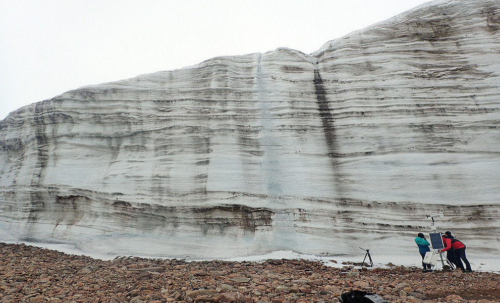 Senkrechte hohe Eiswand auf Grönland, davor sehr klein zwei Gletscherforscher