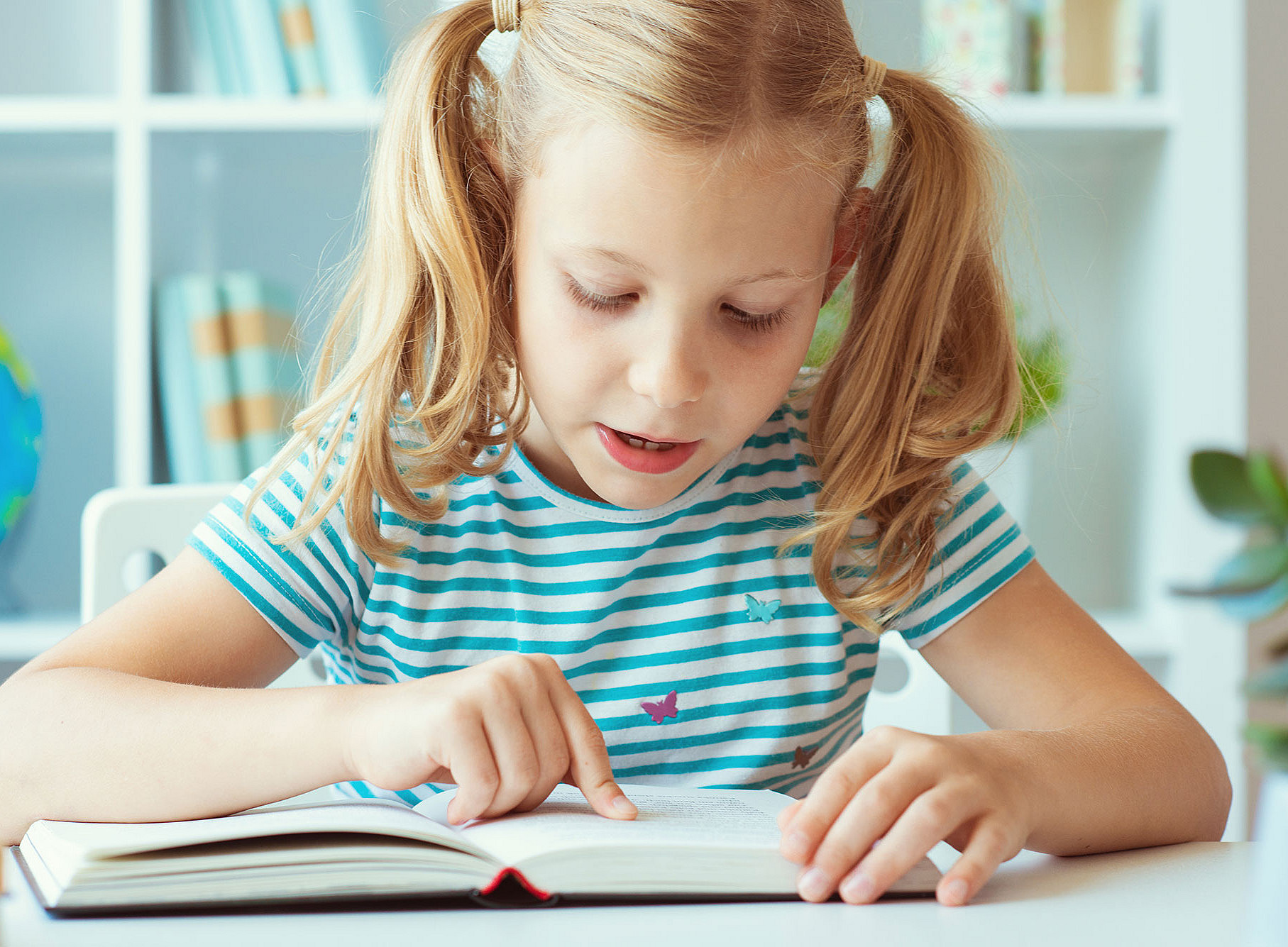 Beginner reader sitting over a book and using her fingers. 