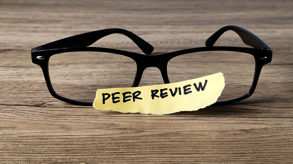 Das Bild zeigt eine Brille und ein Post it mit der Aufschrift "Peer review". ©MohamadFaizal - stock.adobe.com