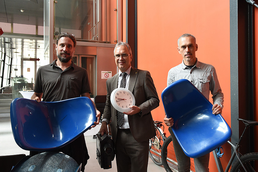 Philipp Jereb (Bundesimmobiliengesellschaft), Rektor Peter Riedler (Uni Graz) und Anton Edelsbrunner (Soziale Arbeit Steiermark) mit Hörsaal-Sesseln, einer Uhr und einem Diaprojektor in der Vorklinik. 