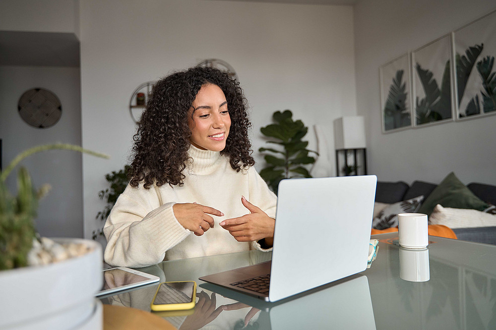 Junge Frau sitzt an einem Schreibtisch und führt ein Videotelefonat über einen Laptop. ©insta_photos - stock.adobe.com