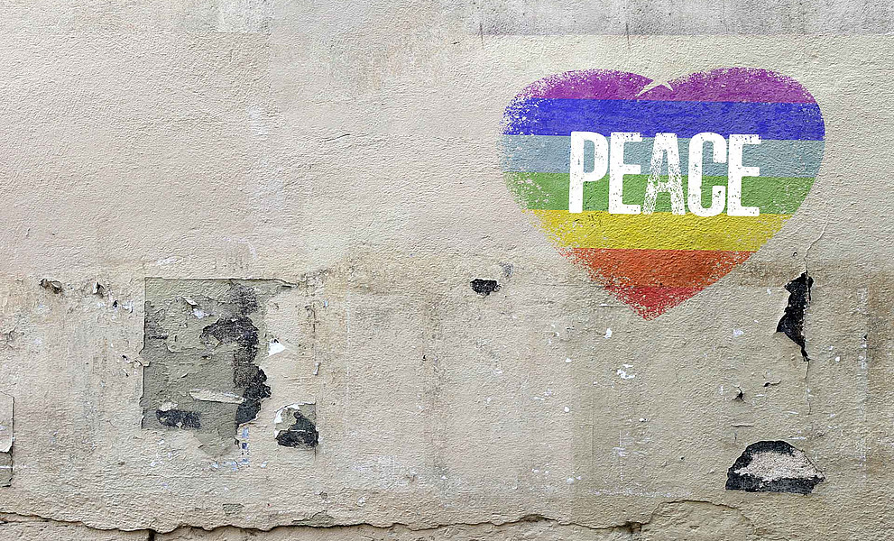 Ein Herz mit Regenbogenfarben und Peace ist aals Graffiti auf eine Mauer gemalt