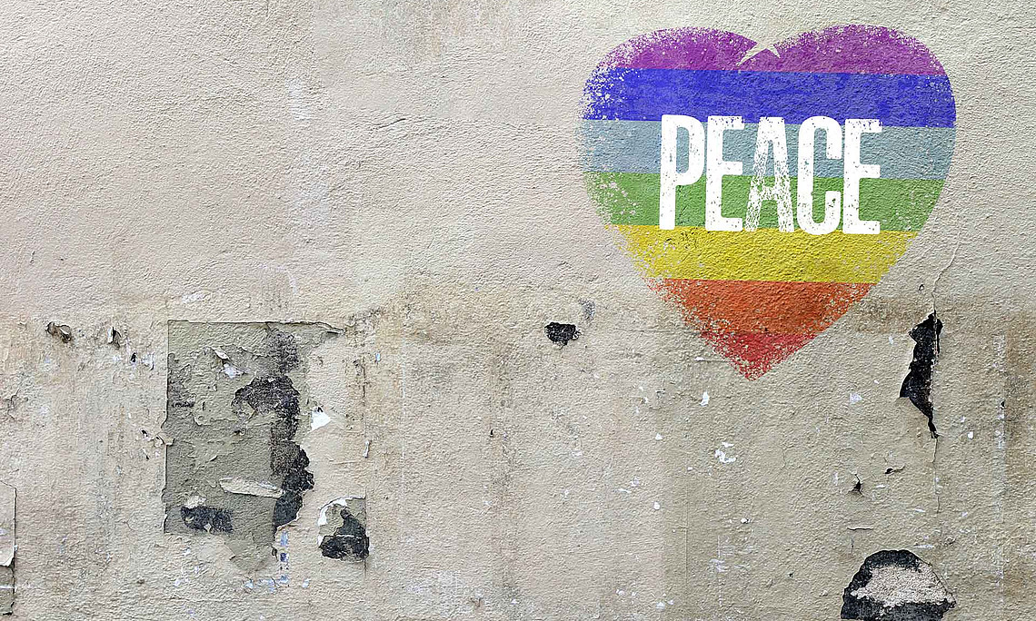 Ein Herz mit Regenbogenfarben und Peace ist aals Graffiti auf eine Mauer gemalt