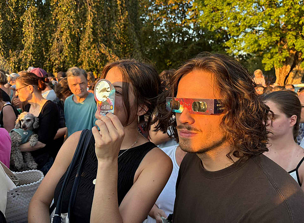eine junge Frau und ein junger Mann schauen mit einer Schutzbrille in die Sonne 