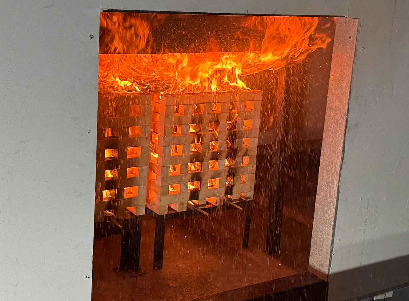Vier Erwachsene in Arbeitskleidung stehen in einer Halle, beobachten einen Feuerwehrmann bei einer Brandschutzübung mit Feuerlöscher. 