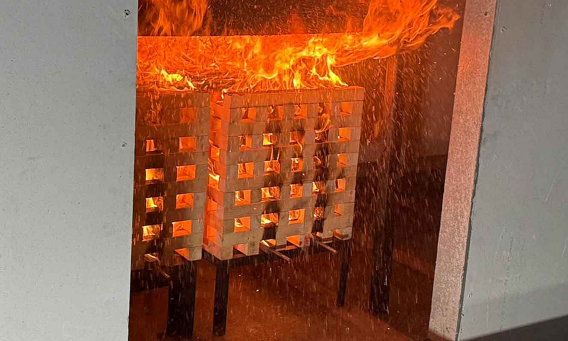 Vier Erwachsene in Arbeitskleidung stehen in einer Halle, beobachten einen Feuerwehrmann bei einer Brandschutzübung mit Feuerlöscher.