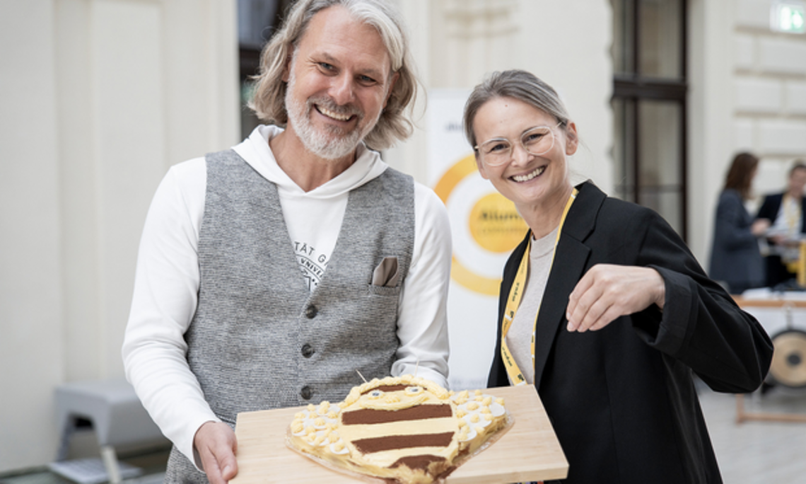 Helmut Jungwirth mit einer Mitarbeiterin der Uni Graz, er hält eine bienenförmige Torte in der Hand