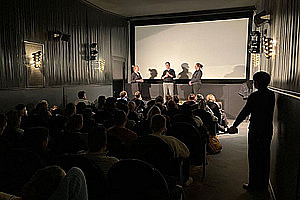 Bild von Kinosaal mit drei Personen im Gespräch vor der Leinwand