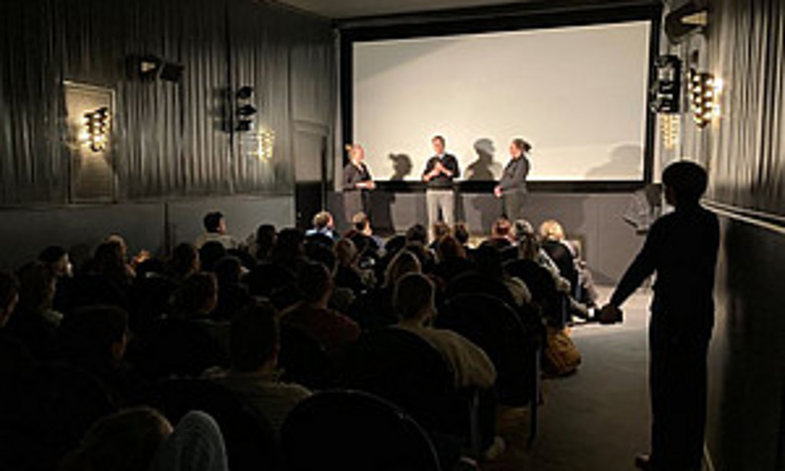 Bild von Kinosaal mit drei Personen im Gespräch vor der Leinwand