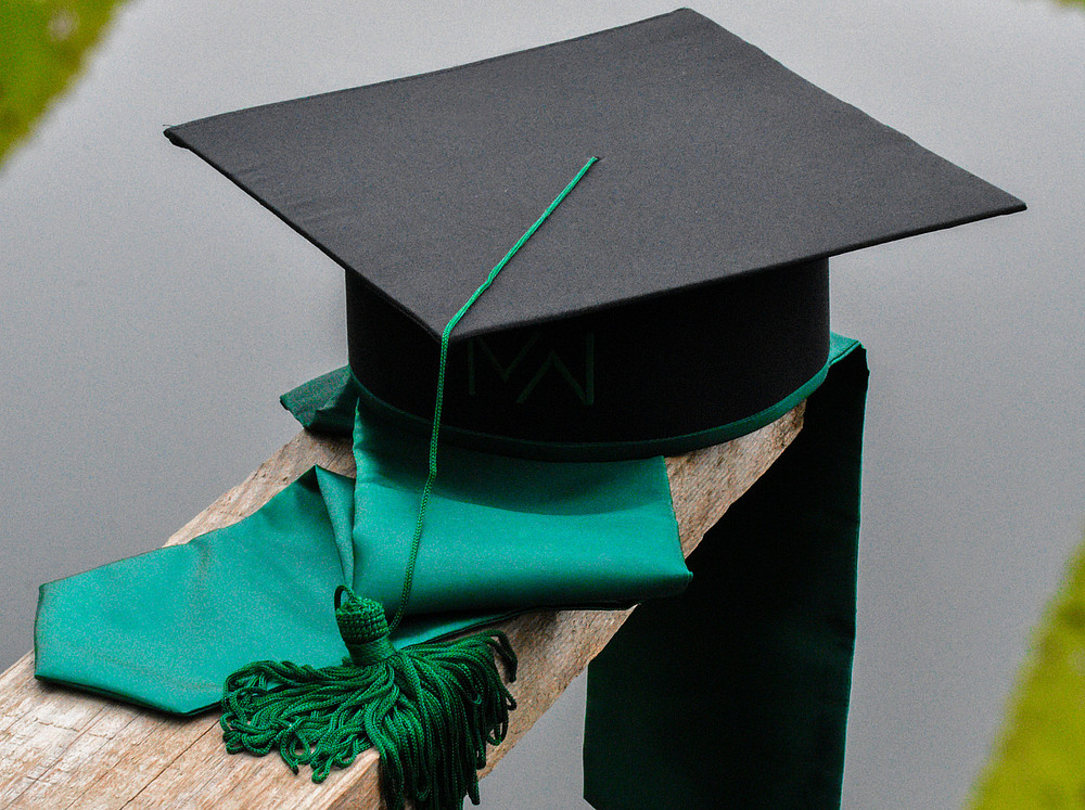 graduation hat on a wooden post with a green sash ©Photo by Dragos Blaga on Unsplash