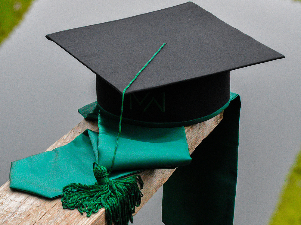 graduation hat on a wooden post with a green sash ©Photo by Dragos Blaga on Unsplash