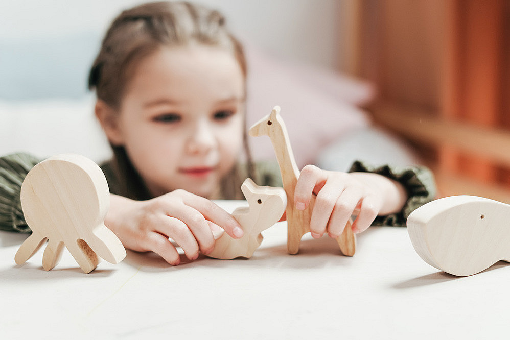 Kinder lernen über Tiere, Mädchen spielt mit Holztieren 