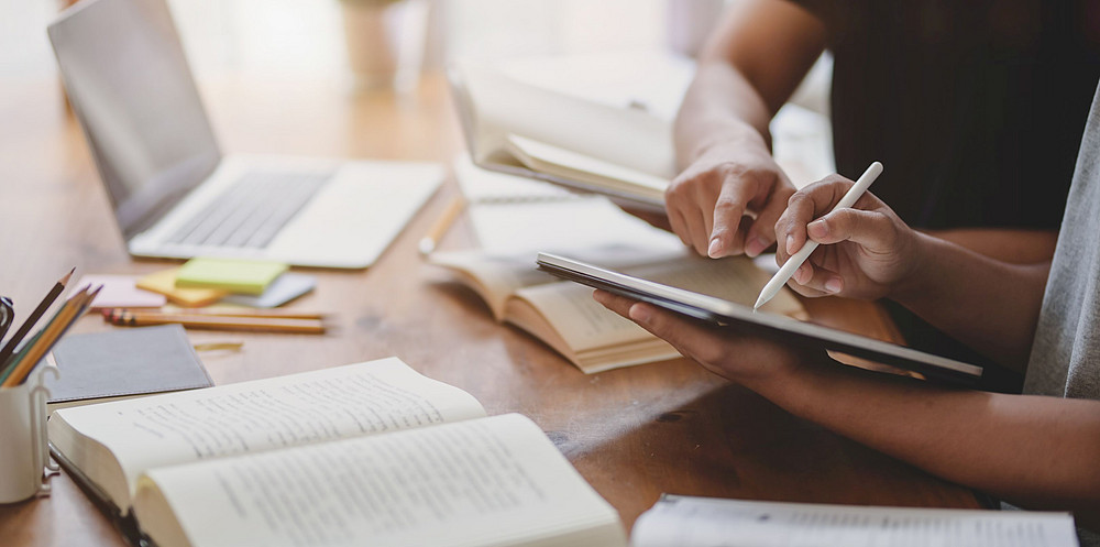 Zwei Personen sitzen an einem Schreibtisch mit Tablet und Büchern ©bongkarn - stock.adobe.com