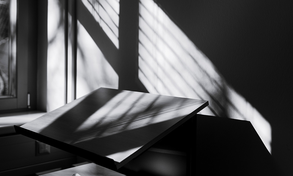 Licht fällt durch ein Fenster auf ein leeres Pult in einem leeren Hörsaal