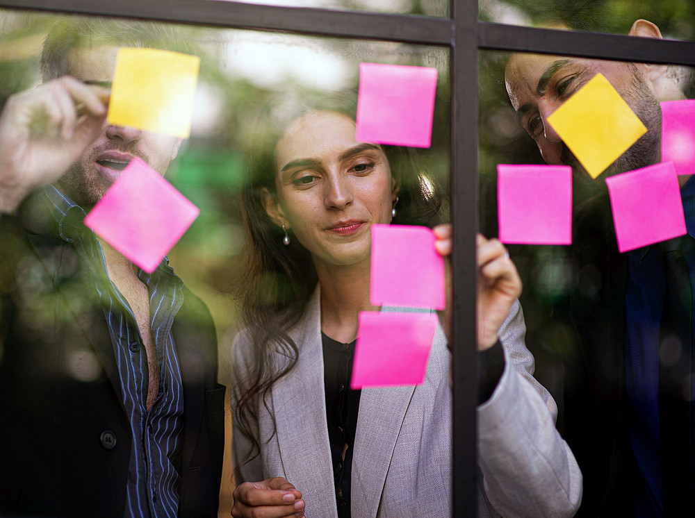 Three people stand in front of a glass wall and write on pink and yellow notes, symbolizing the third-party funded projects at the center. ©SOMPONG DANKHETDAN - stock.adobe.com