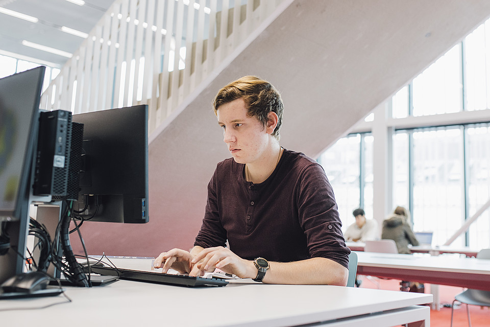 Ein Studierender verwendet einen Computer-Arbeitsplatz in der Universitätsbibliothek