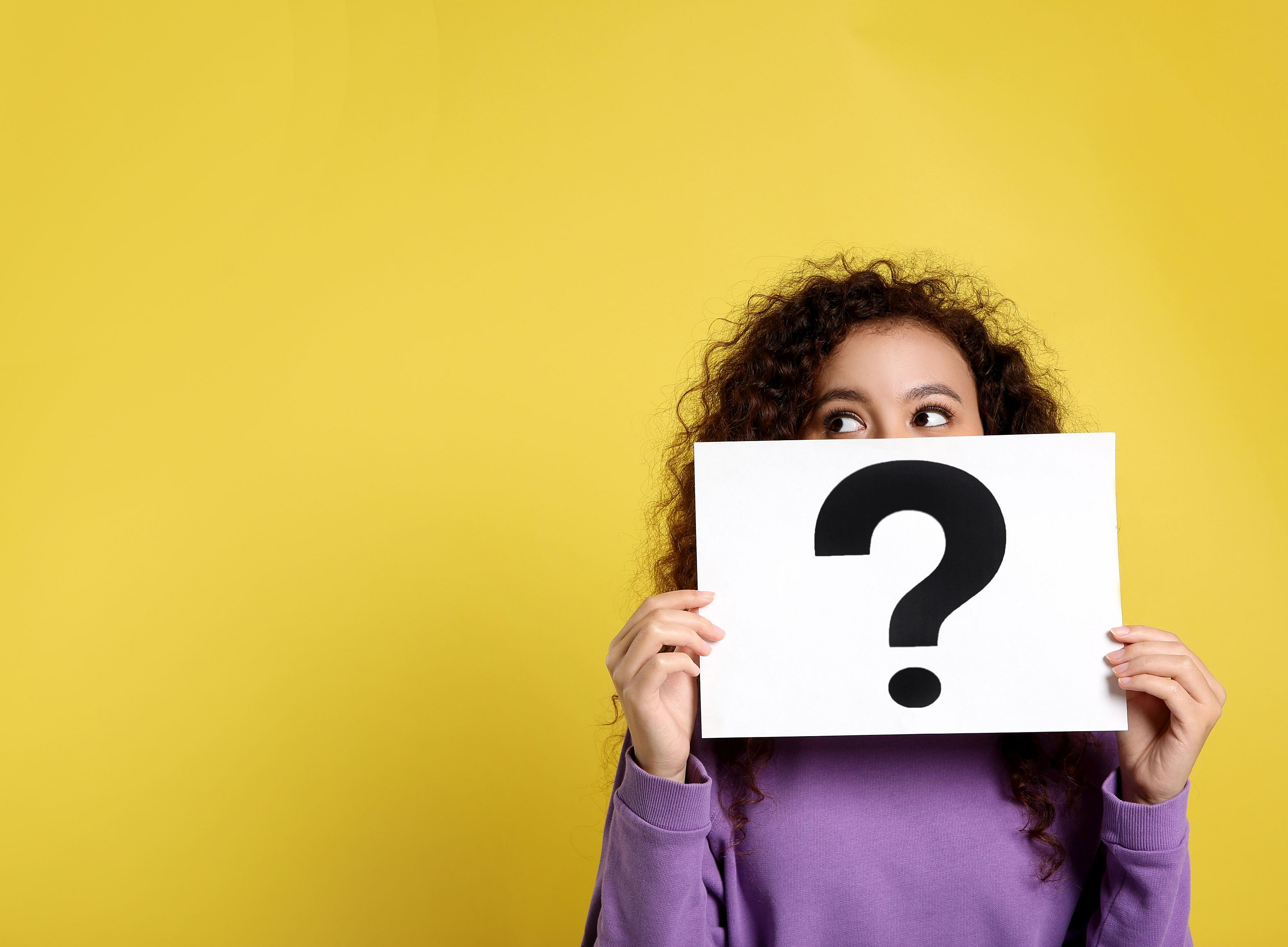 Junge Frau vor gelbem Hintergrund hält ein Schild mit einem Fragezeichen ©Olga Yastremska - stock.adobe.com