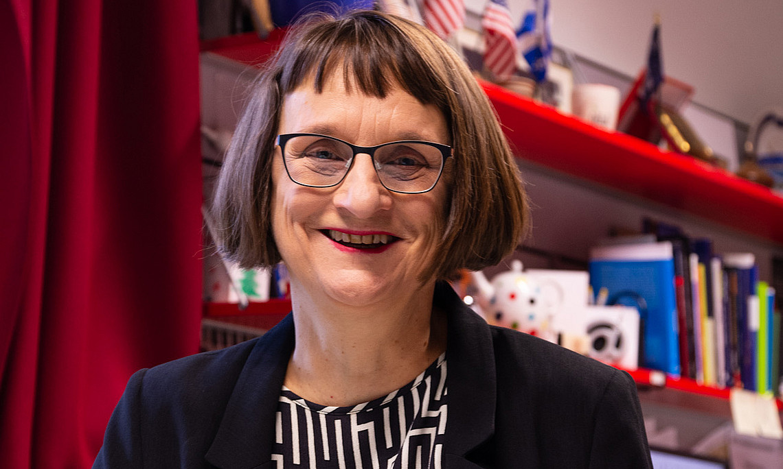 Roberta Maierhofer in front of a board with books and a few small US flags