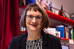 Roberta Maierhofer in front of a board with books and a few small US flags