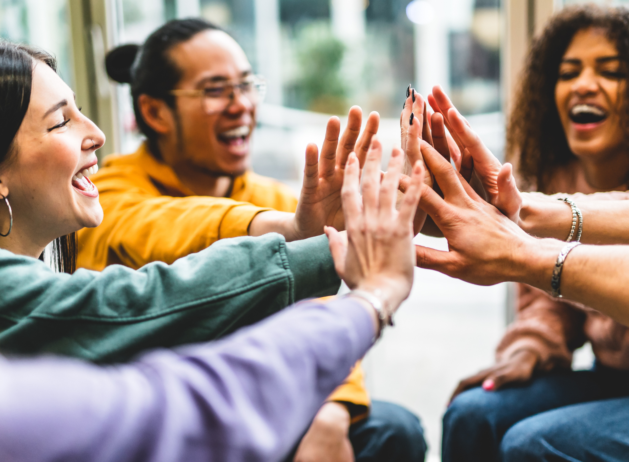 Multiracial happy young people stacking hands-Group of diverse friends having fun unity together indoors at table of community-Human resources Concept Creative and Relationship Youth Culture ©AdobeStock