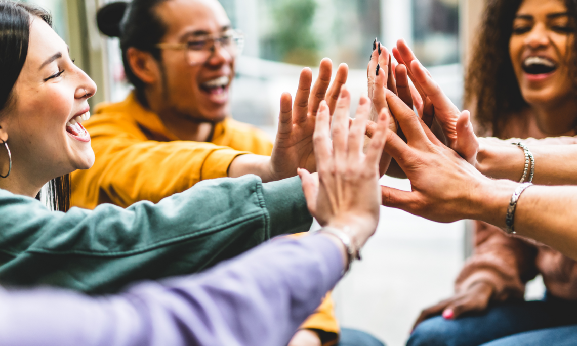 Multiracial happy young people stacking hands-Group of diverse friends having fun unity together indoors at table of community-Human resources Concept Creative and Relationship Youth Culture