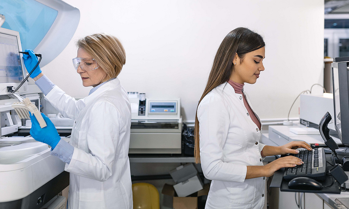 Team von Forschungswissenschaftlerinnen, die am Computer mit medizinischer Ausrüstung arbeiten und Blut- und genetische Materialproben mit speziellen Maschinen im modernen Labor analysieren.