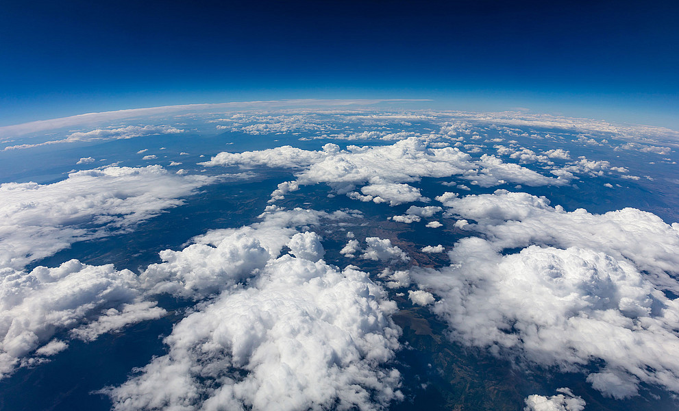 Ausschnitt der Erde von oben, unregelmäßige, weiße Wolkenbänder, blauer Horizont