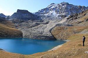 Blockgletscher, der in einen Gebirgssee mündet, schneebedeckter Fels im Hintergrund