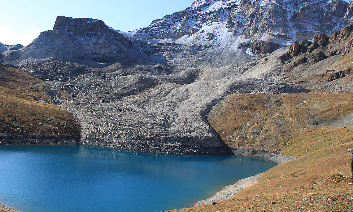 Block glacier flowing into a mountain lake, snow-covered rock in the background