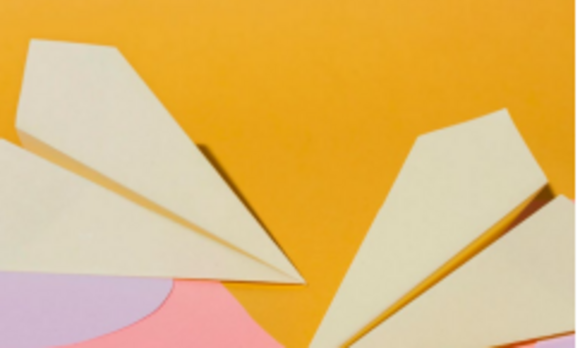 Papierflieger vor orangem Hintergrund