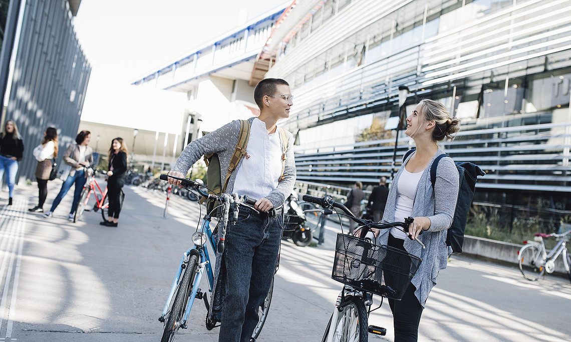 Zwei Studierende mit dem Fahrrad vor dem RESOWI-Zentrum während einer Unterhaltung