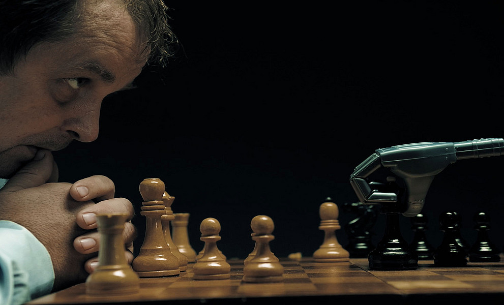 Mann spielt mit einem Roboter Schach und beobachtet beängstigt dessen Zug