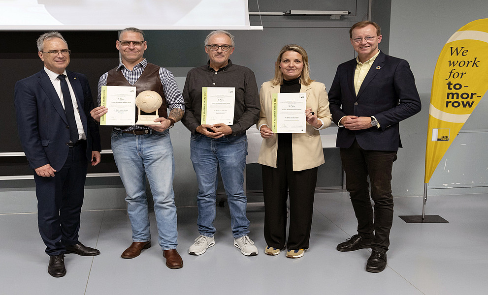 Rektor Peter Riedler, Harald Stelzer, Walter Kurz, Romana Rauter und Gottfried Kirchengast bei der Verleihung des Green Academia Award mit Urkunden, Trophäe und Uni-Graz-Beachflag mit der Aufschrift „we work for tomorrow“