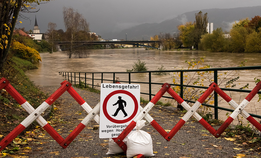 Ein Schild mit der Aufschrift „Lebensgefahr“ wird während des Herbsthochwassers vor einem rot-weiß gestreiften Eisenzaun am überfluteten Fluss Drau in Villach, Österreich, auf den Boden gelegt. 