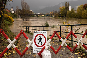 Ein Schild mit der Aufschrift „Lebensgefahr“ wird während des Herbsthochwassers vor einem rot-weiß gestreiften Eisenzaun am überfluteten Fluss Drau in Villach, Österreich, auf den Boden gelegt. 