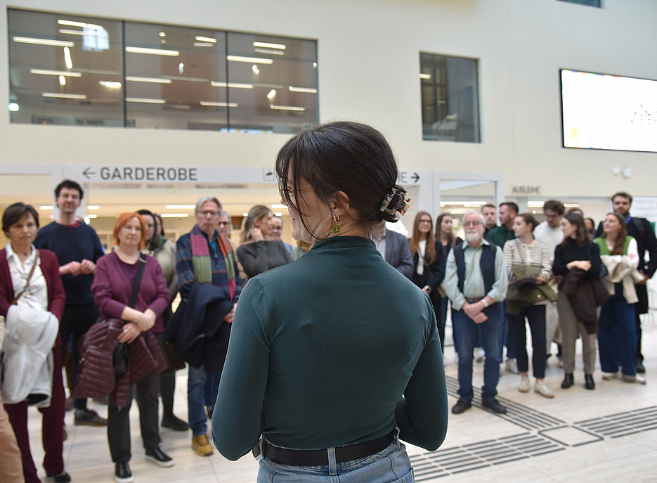 eine frau dreht dre kamera den rücken zu uns spricht zum Publikum 