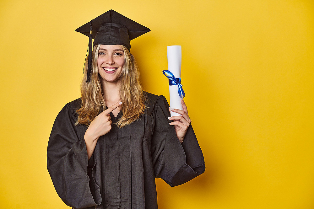 Junge Frau in Abschlussrobe vor gelbem Hintergrund ©Asier - stock.adobe.com