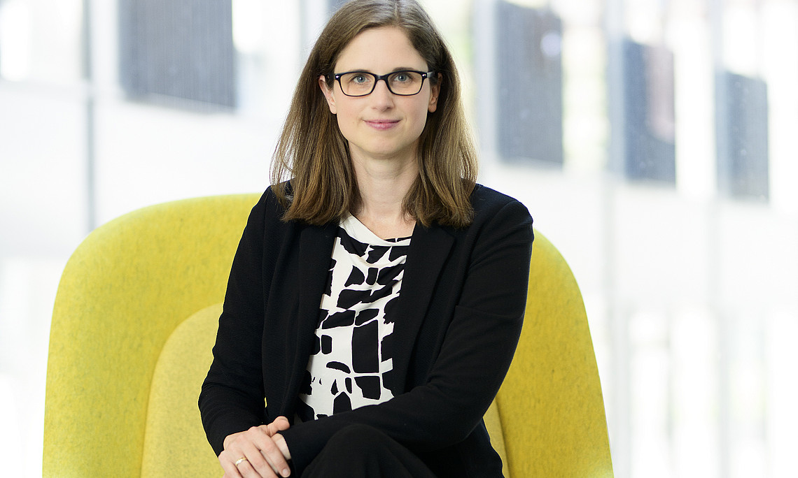Frau Dr. Praprotnik in einem gelben Sessel vor einer Fensterfront