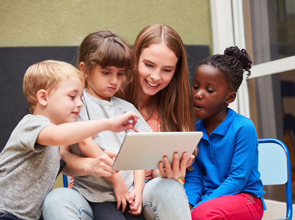 Young woman sitting with children in front of a tablet, symbolizing research at FZIB ©Robert Kneschke - stock.adobe.com