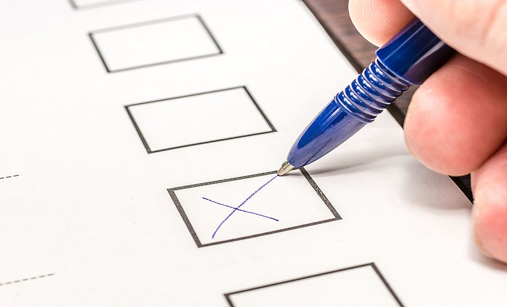 Detail von Hand mit Stift, die ein Kreuz auf einem Wahlzettel macht.