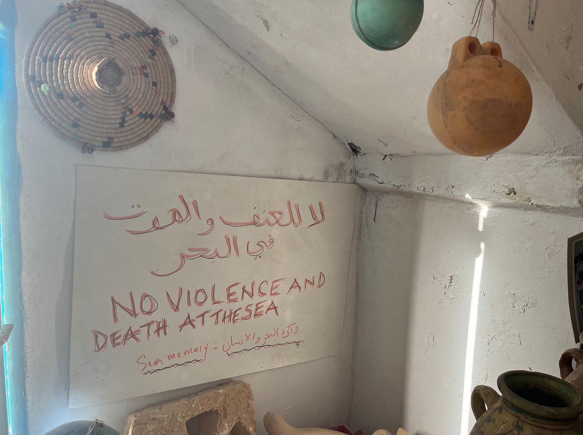 A sign hanging on the wall with the text: "No violence and death at the sea" written both in English and Arabic. ©Private Image by Dr. Chiara Pagano.