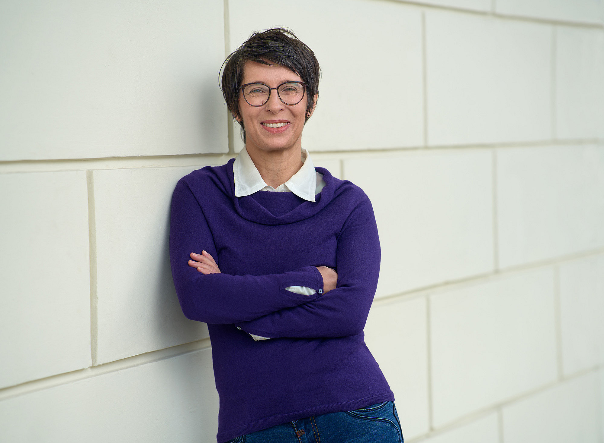 Sabine Bergner leans against a white brick wall ©Uni Graz/wildundwunderbar